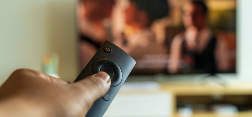 Hotel guest holding a remote control in front of TV, exploring streaming services in their hotel room